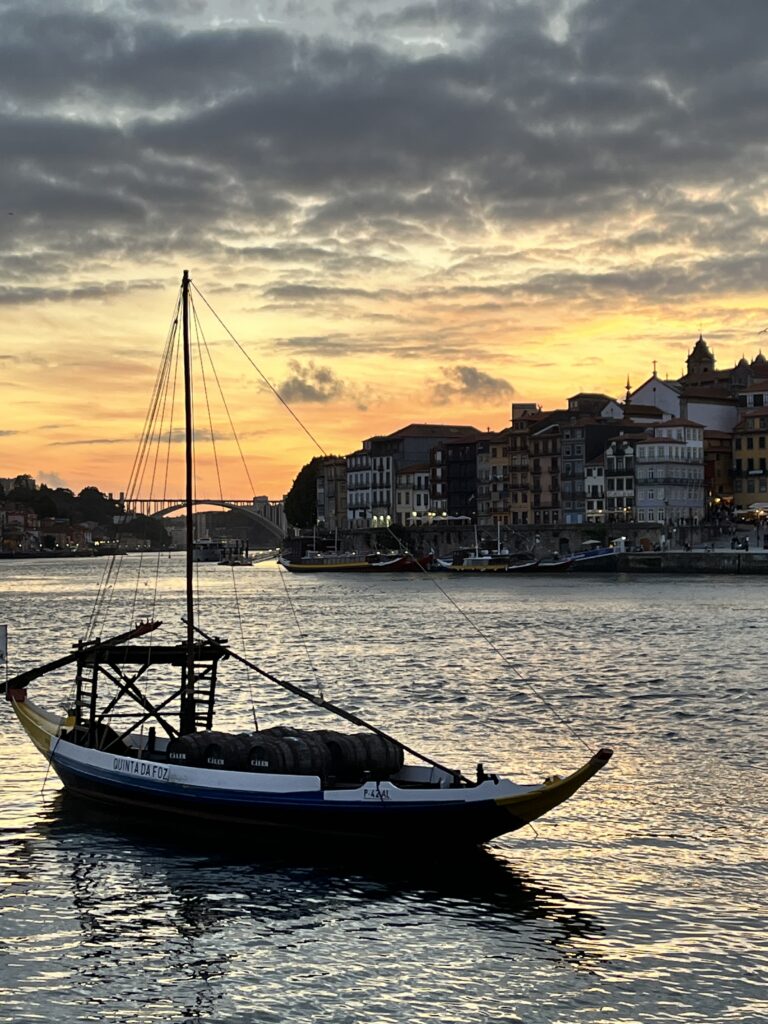 Porto, Portugal by Barbara deBriere. Image of docked sailboat with the douro river and city in the background at sunset.