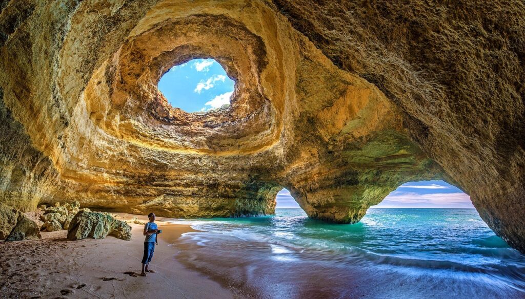 Benagil Caves in Algave, Portugal. Ocean cave formations with a person standing looking up into an opening in the cave.